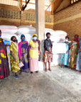 Group of women standing in a warehouse with bags of coffee ready to transport, wearing face masks.