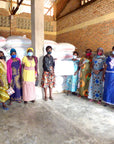 Group of women standing in a warehouse with bags of coffee ready to transport, wearing face masks.