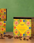 Three boxes of Swelter Coffee with floral designs on a wooden surface with scattered coffee beans, featuring women produced coffee from Latin American countries