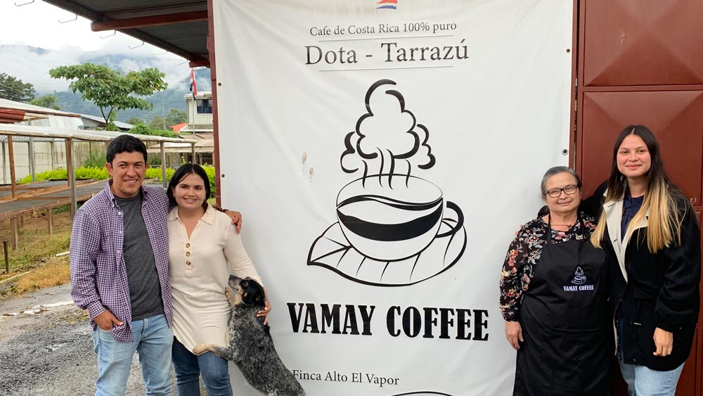 Mayra Solis, her two daughters, and son-in-law smiling next to their coffee sign Vamay Coffee