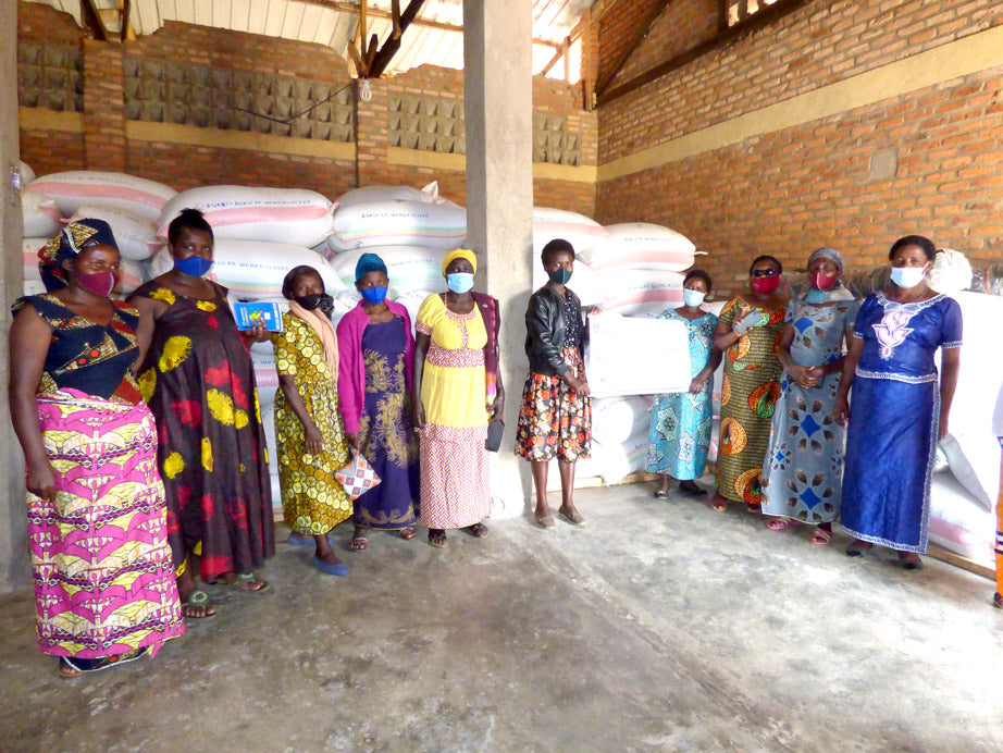 Group of women standing in a warehouse with bags of coffee ready to transport, wearing face masks.