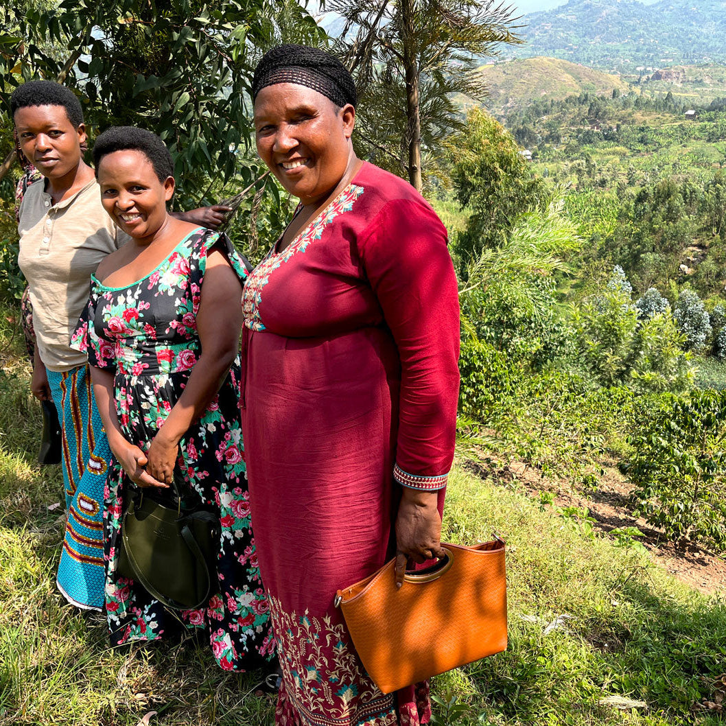 Three women of the Agasake Women standing together with the women's coffee farm in the distance