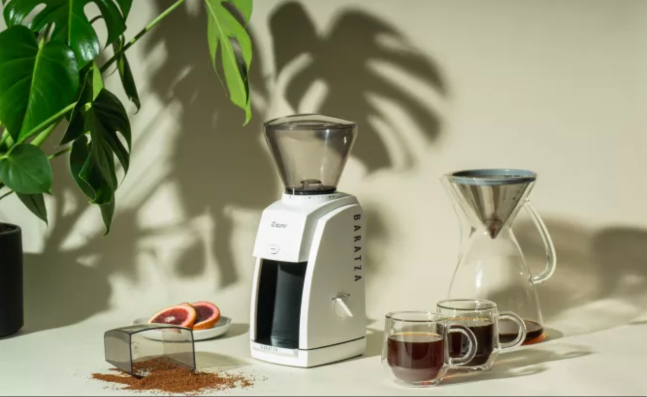 A white Baratza Encore grinder on a white table with coffee mugs next to it