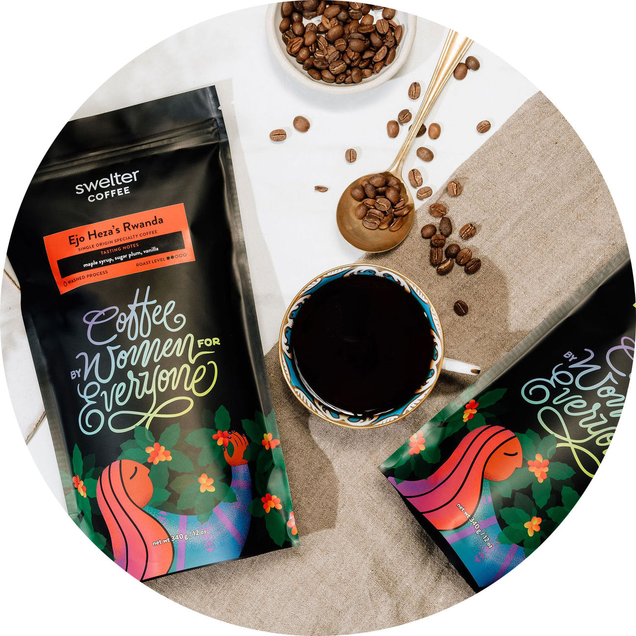 Overhead view showing 2 coffee bags of ethically sourced coffee, with a cup of brewed coffee in between, and coffee beans scattered on the table