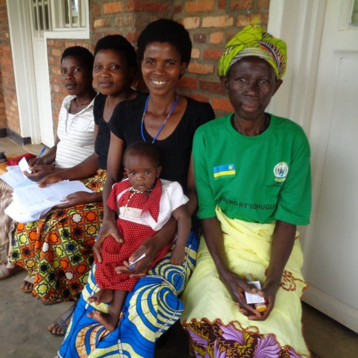 Four women farmers in Rwanda seated in front of a house, one woman with a baby.