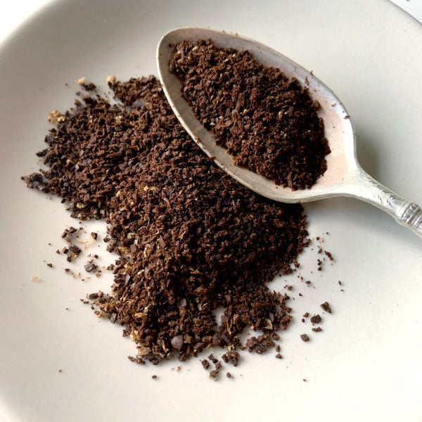 A close up view of coarsely ground coffee, where the grains look close to coarse seas salt, on a white plate with a spoon. 