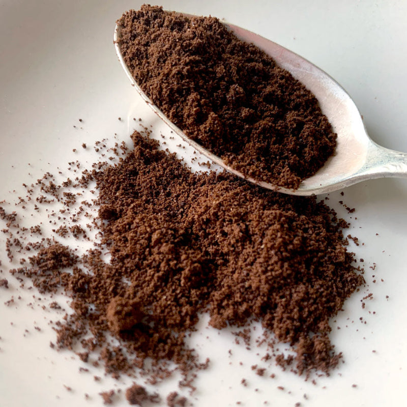 A close up view of finely ground coffee, where the grains look closer to spices where they just start to clump, on a white plate with a spoon. 