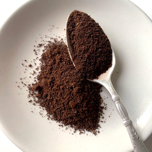 A close up view of medium ground coffee, where the grains look close to table salt, on a white plate with a spoon. 