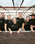 Mayra Solis and her family in their dry mill behind a bed of drying coffee beans