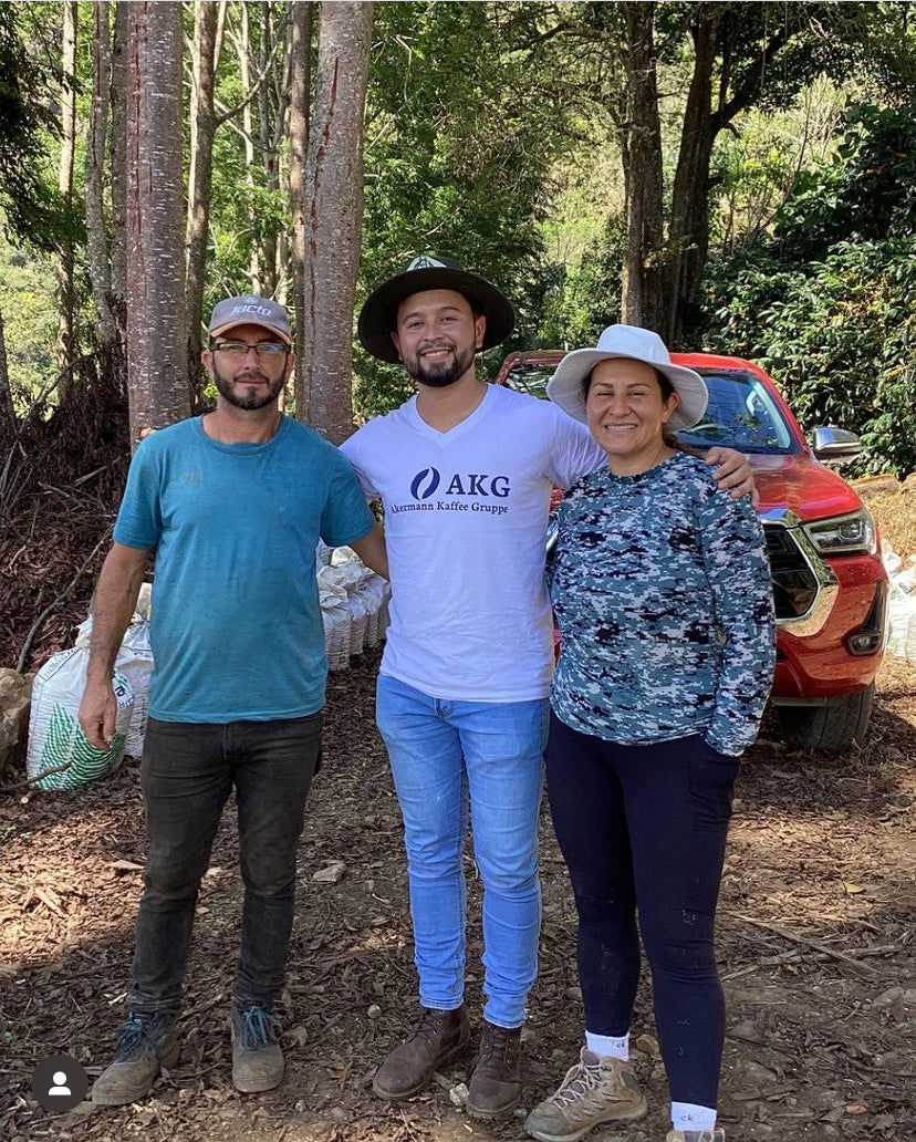 Woman coffee producer Seilyn Jimenez with two men on her farm in Costa Rica in front of a red truck.