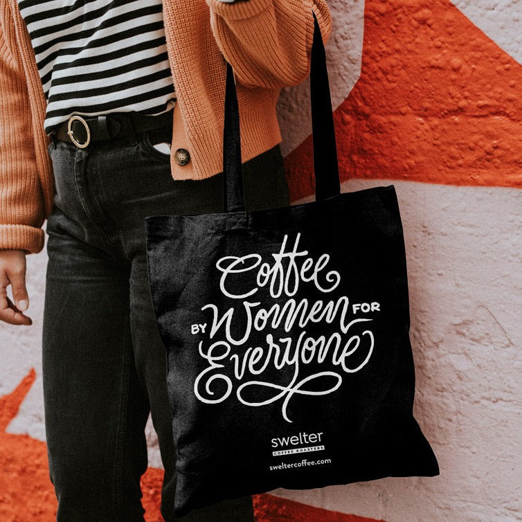 Close up view of Swelter Coffee's branded tote bag, held by a person in front of a graphic wall