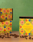 Three boxes of Swelter Coffee with floral designs on a wooden surface with scattered coffee beans, featuring women produced coffee from Latin American countries