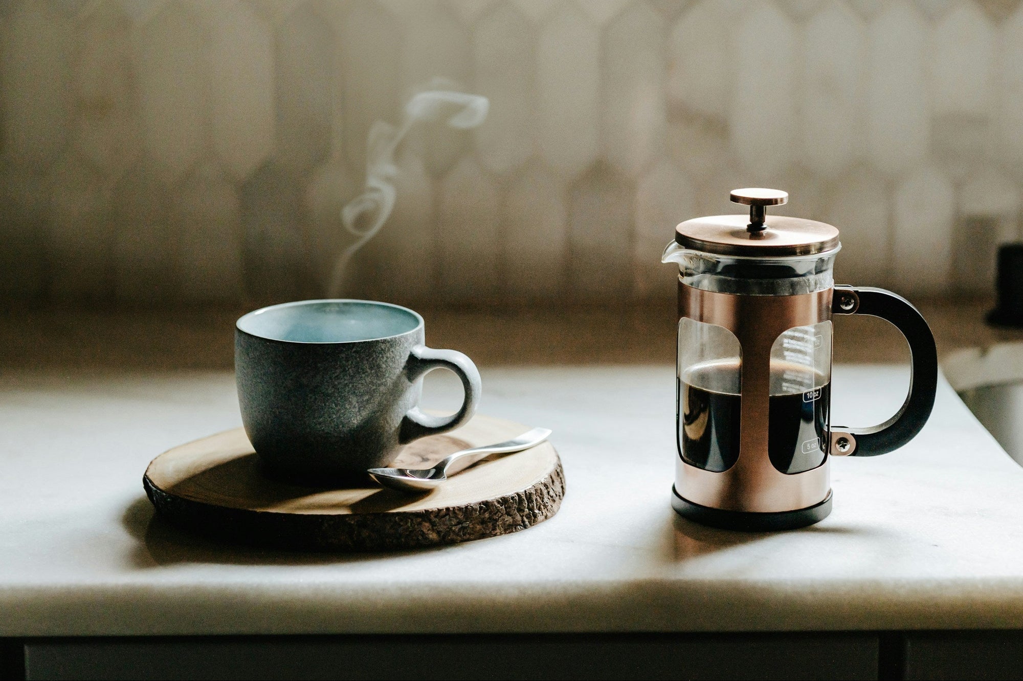 A french press brewing coffee on a table next to a coffee mug