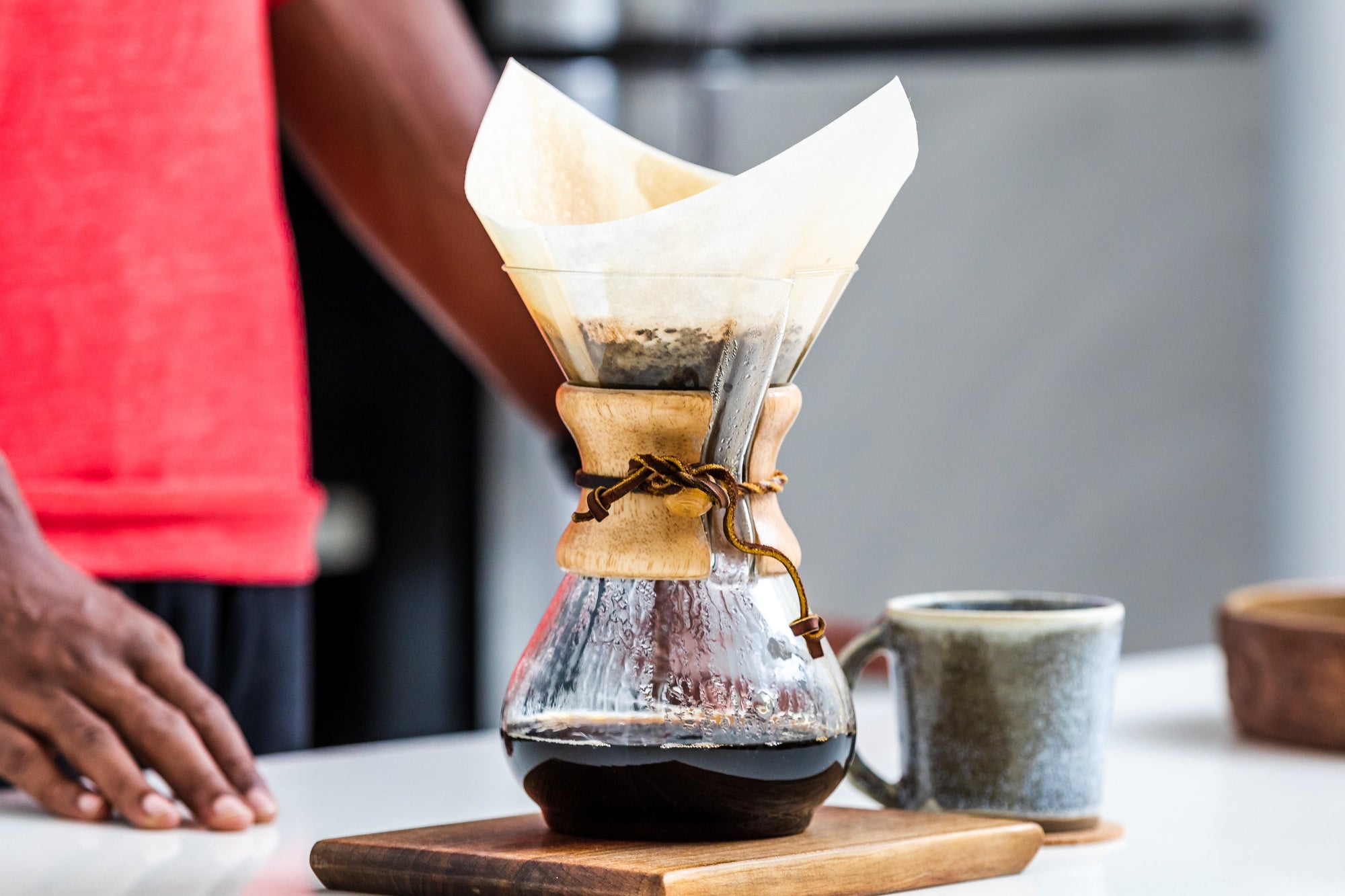 A man standing next to a Chemex coffee brewer as it brews a fresh cup of coffee